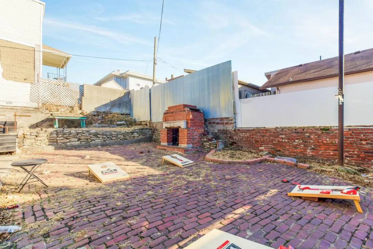 An outdoor space with a rustic brick oven, cornhole boards set up for play, and a cobblestone path weaving through. The area is built for both social gatherings and relaxing evenings, offering a lively, communal atmosphere accentuated by games and outdoor cooking.