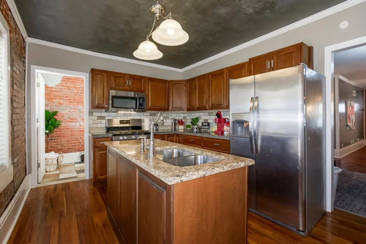 A modern kitchen interior featuring a spacious granite countertop, stainless steel appliances, and wooden cabinets. The space is welcoming and functional, set up for both cooking and socializing, with ample room for meal preparation and gathering.