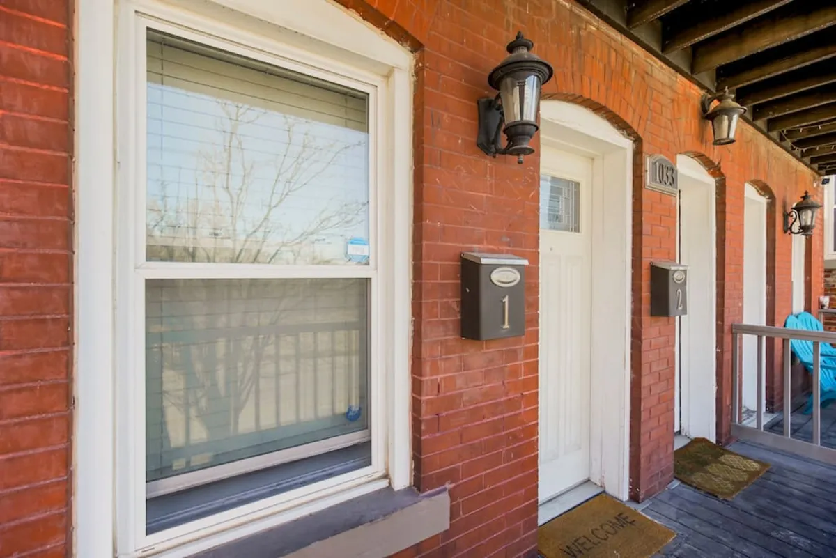 An exterior shot of the building’s facade with prominent brickwork, clear door numbers, a welcome mat, and outdoor seating, suggesting a friendly, approachable atmosphere ideal for relaxing after work or informal meetings with colleagues.
