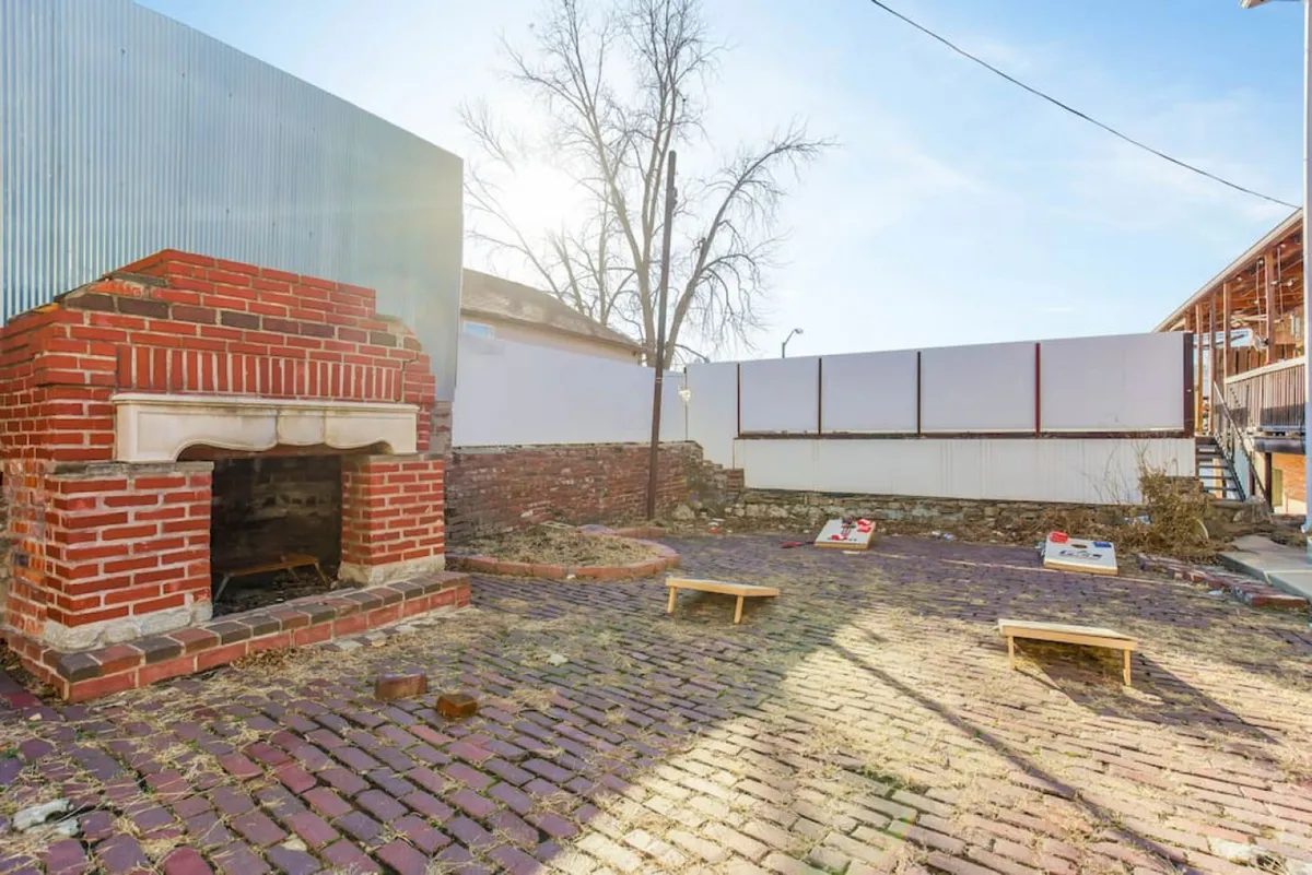 A playful exterior scene with a brick fireplace, cornhole boards on a textured brick patio, and ample space for outdoor games and gatherings. The atmosphere is lively yet relaxed, hinting at memorable moments shared with friends.