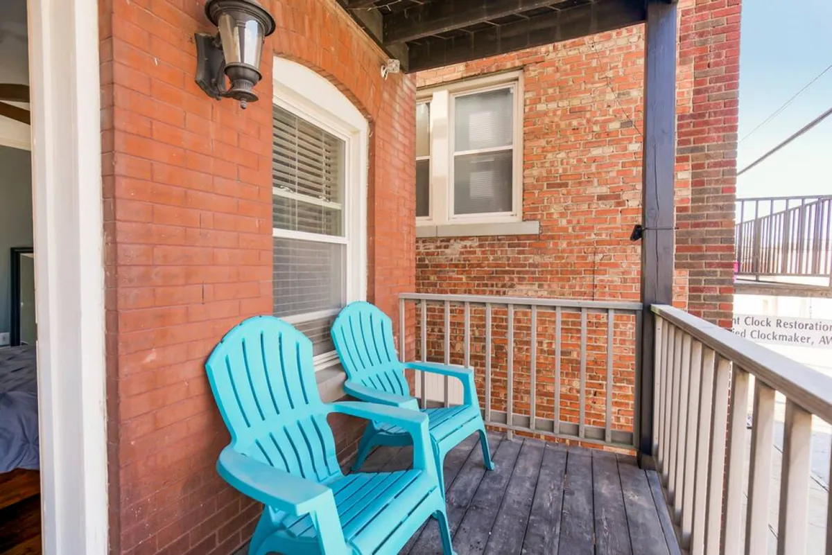 A set of blue Adirondack chairs gather on a small patio framed by a brick wall and wooden railing. The space is designed for relaxation, socializing, or enjoying a morning coffee, with an open-air feel that connects the home to the surrounding neighborhood.