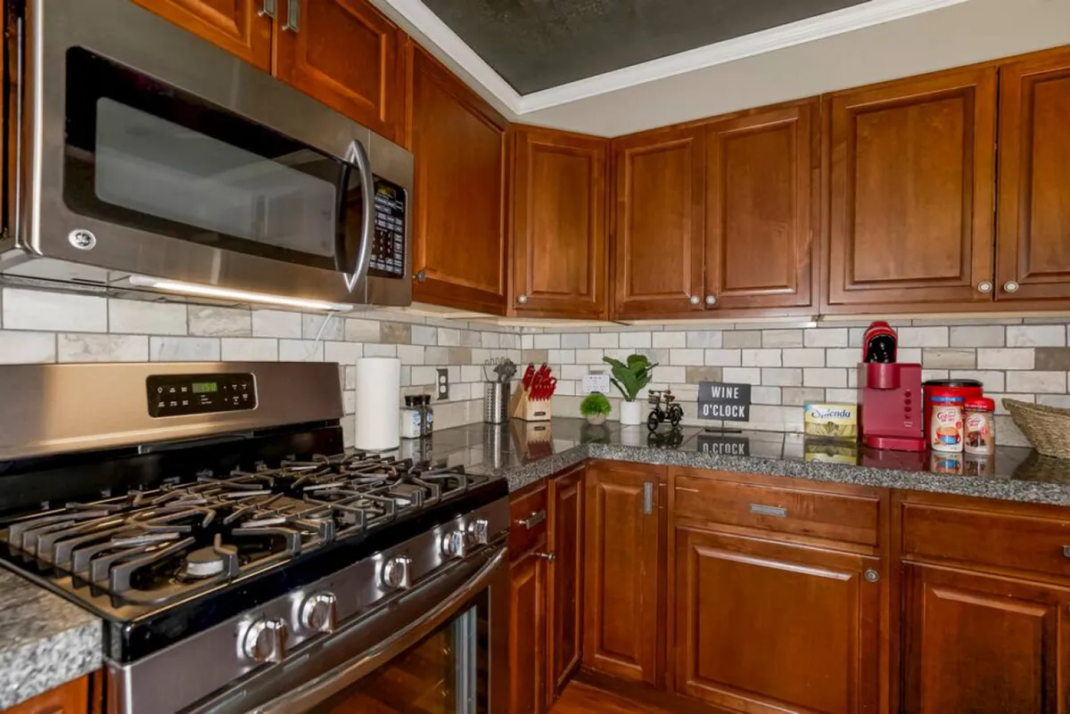 A close-up view of the kitchen area featuring a stainless steel microwave, gas stove, granite countertop, and wooden cabinets. Decorative items on the counter suggest everyday usability and warmth, ideal for preparing meals and entertaining guests.
