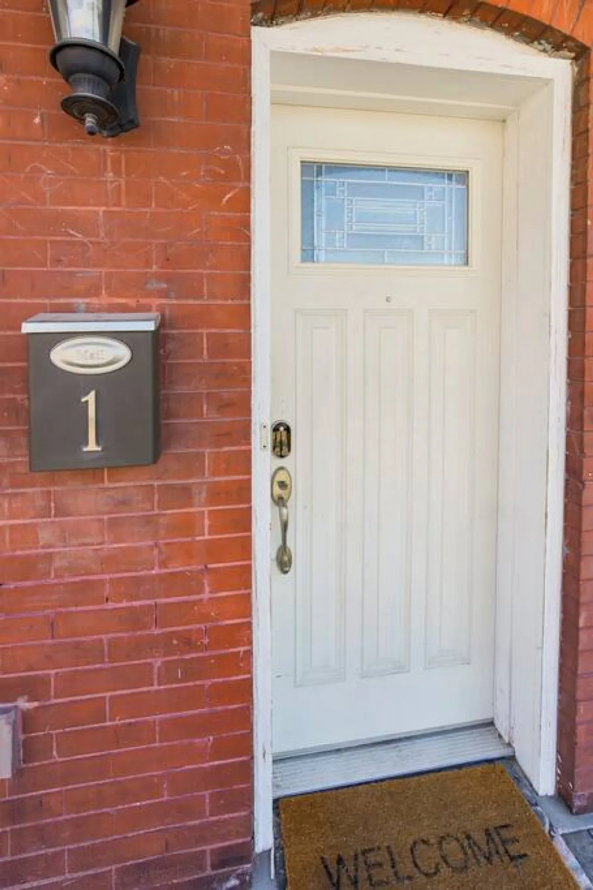 This image shows the inviting front entryway to the home, featuring a nicely maintained brick facade, a front door with a welcome mat, and a visible mailbox. The entryway is clean and approachable, projecting a sense of arrival and security.
