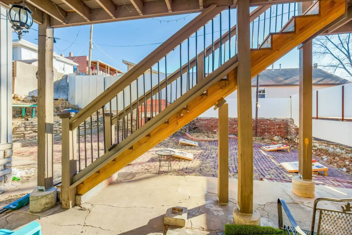 An inviting outdoor space featuring a wooden staircase, brick flooring, comfortable seating, and lush landscaping. The scene is set for social gatherings, barbecues, or relaxing after an event-filled day in the city.